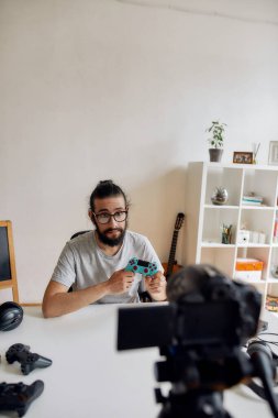 Evde yeni cihazlar hakkında video blogu veya video blogu kaydederken oyun denetleyicisini gösteren, elinde tutan gözlüklü bir erkek teknoloji blogcusu