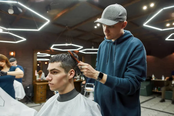 Moda saç kesimi yaptırıyorum. Modern berber dükkanında yakışıklı bir adamın saçını kurutan profesyonel bir berberin yan görüntüsü. — Stok fotoğraf
