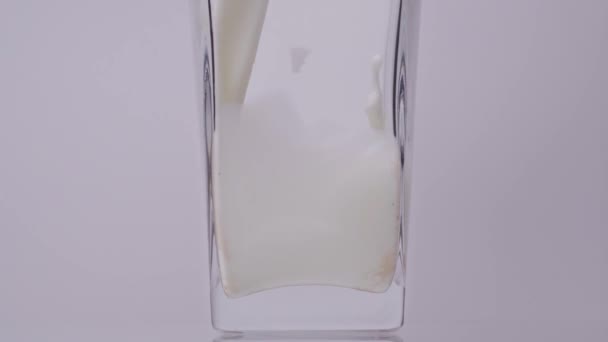 Mleko jest konieczne. Super slow motion shot wylewania, pluskając świeże mleko do przezroczystej szklanki na białym tle. Zamknij drzwi. Koncepcja przetworów mlecznych — Wideo stockowe