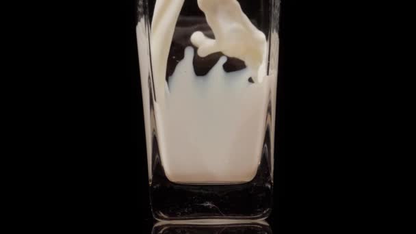 Πιείτε δροσερό. Σούπερ αργή κίνηση shot του ρίχνει, πιτσιλίζει φρέσκο γάλα σε ένα διαφανές γυαλί σε μαύρο φόντο. Κλείσε. Έννοια γαλακτοκομικών προϊόντων — Αρχείο Βίντεο