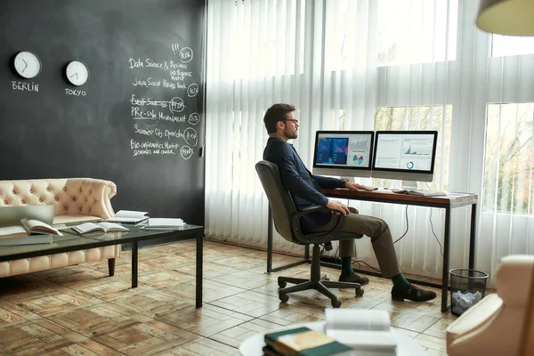 Analista financiero en el trabajo. Hombre de negocios concentrado con anteojos sentados en la oficina moderna, mirando gráficos y gráficos en la pantalla de la PC, analizando datos estadísticos — Foto de Stock