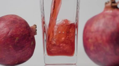 Sağlığa öncelik verin. Şeffaf bir bardağa nar suyu ve beyaz arka plana iki nar dökerek süper yavaş çekim yapıyoruz. Kapatın. Sağlıklı içecek, vitaminler, meyve konsepti