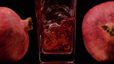 Lezzetli. Şeffaf bir bardağa nar suyu dökerken süper yavaş çekim ve siyah arka plana karşı iki nar. Kapatın. Sağlıklı içecek, vitaminler, meyve konsepti