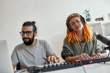 Rastalı kadın şarkı söylüyor ve çalıyor. Kadın ve erkek blogcu sentezleyici, davul çalar ve dizüstü bilgisayar kullanarak müzik yapıyor, video blogu veya vlog kaydediyor