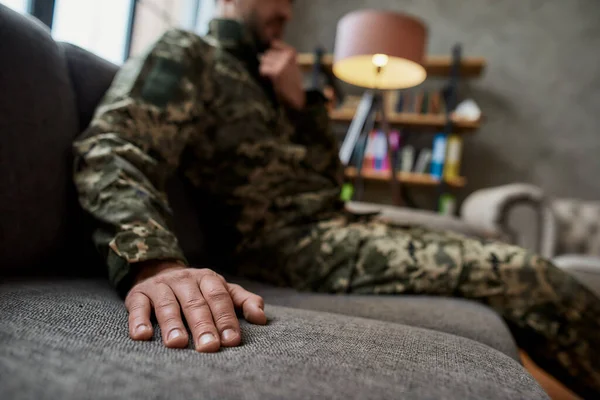 Close-up van de hand van militair in camouflage zittend op de bank tijdens therapiesessie. Soldaat lijdt aan depressie, psychologisch trauma. PTSS-concept — Stockfoto