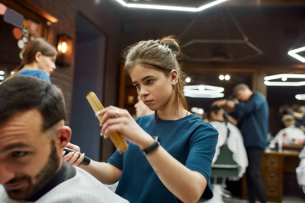 Close-up shot van een professionele kapper meisje of vrouwelijke kapper werken met een tondeuse, het maken van trendy kapsel voor een knappe bebaarde man — Stockfoto