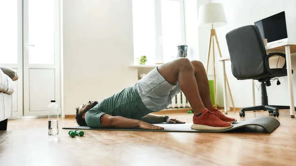 Γυμνάζομαι. Νεαρός ενεργός άνδρας κάνει ασκήσεις κατά τη διάρκεια της πρωινής άσκησης με αλτήρες στο στρώμα γιόγκα στο σπίτι. Αθλητισμός, υγιεινός τρόπος ζωής — Φωτογραφία Αρχείου