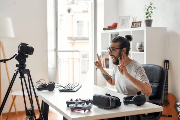 Hombre blogger tecnología mostrando signo de paz para los suscriptores durante la grabación de blog de vídeo o vlog sobre nuevos gadgets en el estudio en casa —  Fotos de Stock