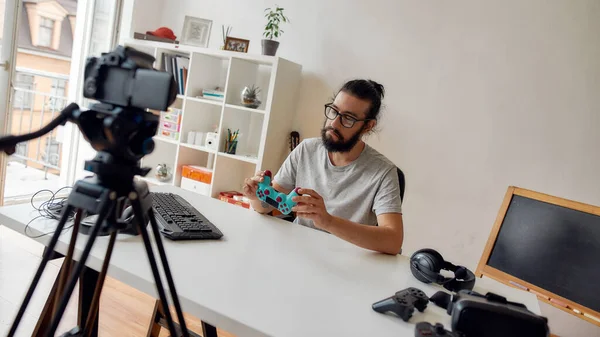 Hombre blogger de tecnología en gafas mirando el joystick controlador de juego, sosteniéndolo mientras graba video blog o vlog sobre nuevos gadgets en casa — Foto de Stock