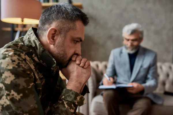 Hulp nodig. Militaire man van middelbare leeftijd op zoek bedachtzaam tijdens therapie sessie met psycholoog. Soldaat lijdt aan depressie, psychologisch trauma. PTSS-concept — Stockfoto