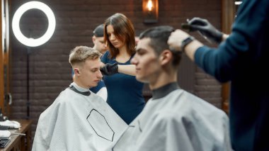 Berber dükkanındaki insanlar. Genç odaklı berber kız ya da bayan kuaför müşteriler için yeni moda saç kesimi yapıyor.