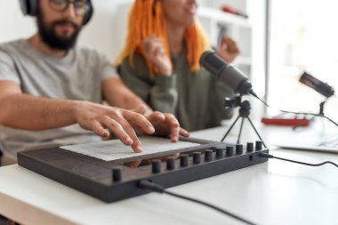 Ses yaratıyorum. Teçhizat ve trampet makinesiyle müzik yapan bir adamın ellerine yakın çekim. Kadın ve erkek blogcular evde video blogu veya vlog kaydediyor