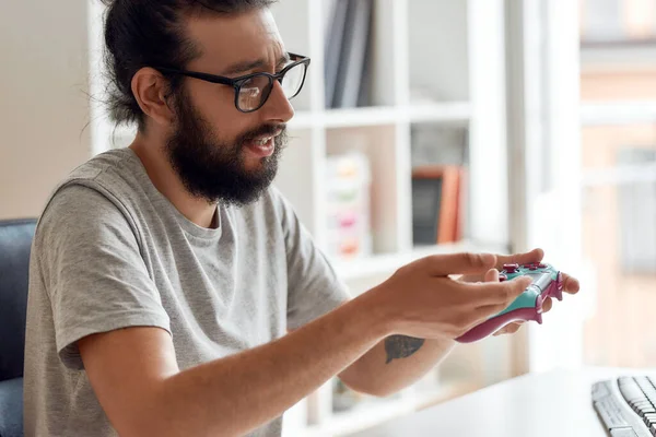 Hombre blogger de tecnología en gafas mirando el joystick controlador de juego, sosteniéndolo mientras graba video blog o vlog sobre nuevos gadgets en casa — Foto de Stock