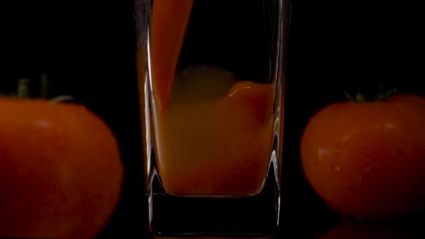 Налей еще. Супер замедленная съемка наливания томатного сока в прозрачный стакан и двух помидоров на черном фоне. Закрывай. Здоровый напиток, витамины — стоковое видео