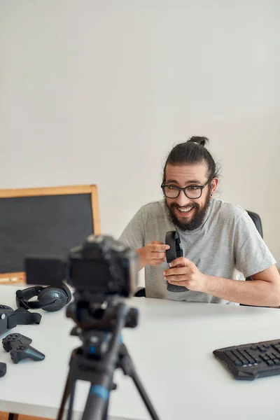 Man teknik bloggare i glasögon ser upphetsad, håller och visar hörlurar medan du spelar in video blogg eller vlog om nya prylar hemma studio — Stockfoto