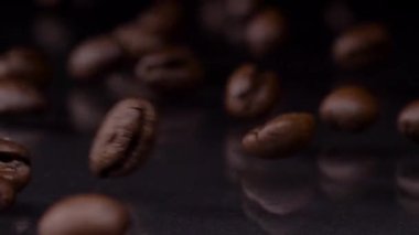 Pahalı bir zevk. Kahverengi kahve çekirdekleri yuvarlanırken, ahşap masaya düşerken, arka planda koyu renk. Kahve taneleri 4K videosunu kapatır