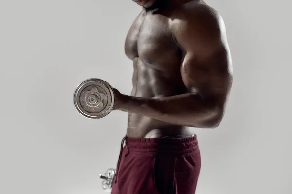 Gehakt schot van jonge gespierde Afro-Amerikaanse man die gewichten tilt, geïsoleerd boven grijze achtergrond. Sport, workout, bodybuilding concept — Stockfoto