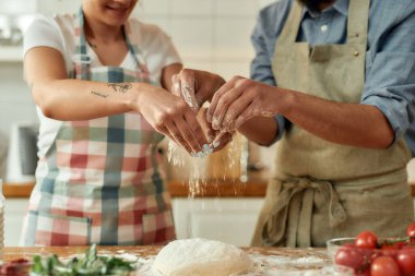 Çiftin hamuru hazırlarken kesilen görüntüsü. Önlüklü genç adam ve kadın evde pizza yapıyor. Hobi, yaşam tarzı
