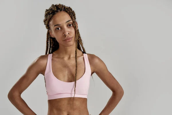 Retrato de una joven mujer de raza mixta deportiva en ropa deportiva mirando a la cámara mientras posa aislada sobre un fondo gris. Estilo de vida saludable y concepto deportivo — Foto de Stock