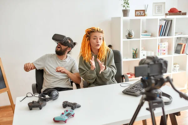 Hombre usando anteojos vr, mientras mujer hablando con la cámara. Joven blogger de tecnología masculina y femenina grabando video blog o vlog sobre nuevos gadgets en casa —  Fotos de Stock