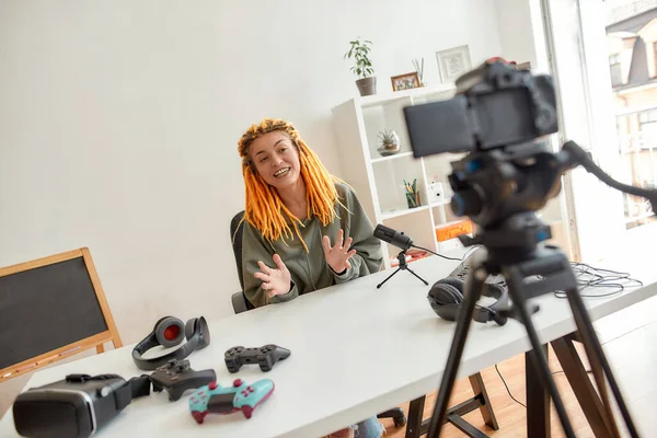Blogger de tecnología femenina con rastas sonriendo y hablando mientras graba video blog o vlog sobre nuevos gadgets en casa —  Fotos de Stock