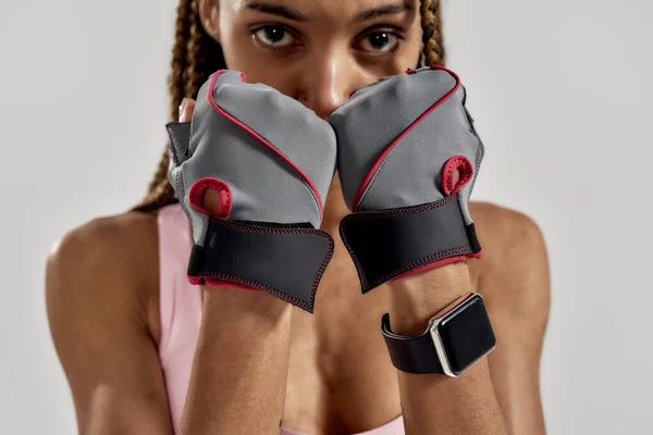 Retrato recortado de jovem mulher de raça mista esportiva em sportswear olhando para a câmera, vestindo luvas de fitness enquanto posando isolado sobre fundo cinza. Estilo de vida saudável e conceito de esportes — Fotografia de Stock