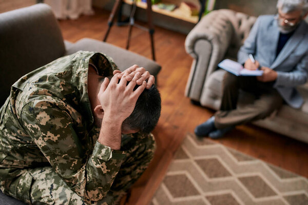 Remove your memories. Middle aged military man holding his head in pain and depression during therapy session with psychologist. Soldier suffering from psychological trauma. PTSD concept