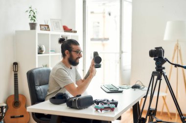 Erkek teknoloji blogcusu elinde kulaklık tutuyor, video blogu ya da video blogu kaydederken başparmaklarını gösteriyor.