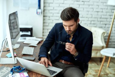 Genç konsantre iş adamı, finans analisti veya satış müdürü işyerinde oturuyor ve dizüstü bilgisayar üzerinde çalışıyor, istatistiksel verileri analiz ediyor