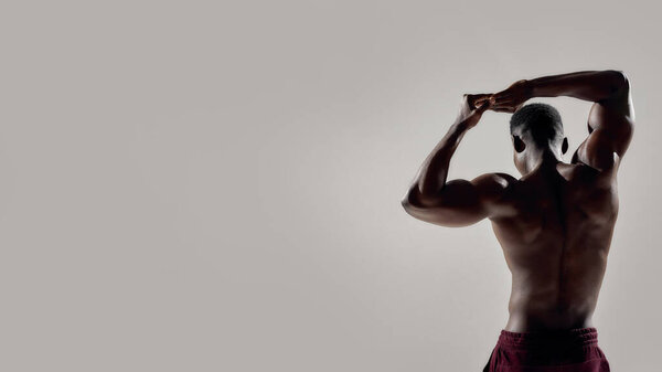 Well built. Rear view of a young muscular african american bodybuilder raising his arms while posing shirtless isolated over grey background. Sports, workout, bodybuilding concept. Web Banner