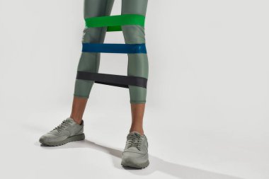 Daha güçlü bacaklar için. Spor yapan, spor yapan kadınların bacak egzersizlerine yakın çekim. Gri arka planda üç elastik bant var. Sağlıklı yaşam tarzı ve spor anlayışı