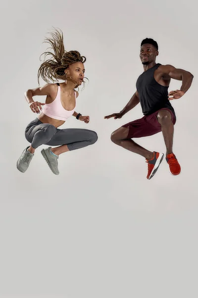 Full length shot of young muscle african american man and sportive mixed race woman jumping, γιορτάζοντας το μεγάλο επίτευγμα, χαρά απομονωμένη πάνω από γκρι φόντο — Φωτογραφία Αρχείου