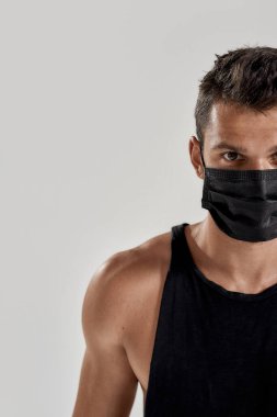 Siyah tıbbi maske takmış beyaz bir adamın gri arka planda tek başına kameraya bakarken yarı yüz portresi. Sağlık, spor, karantina konsepti