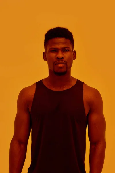 Jovem musculoso afro-americano olhando para a câmera, posando isolado sobre fundo laranja. Esportes, treino, conceito de musculação — Fotografia de Stock