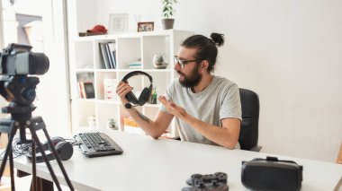 Erkek teknoloji blogcusu elinde kulaklık tutarken video blogu veya video blogu kaydediyor.