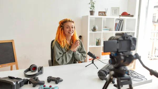 Female technology blogger with dreadlocks smiling and talking while recording video blog or vlog about new gadgets at home