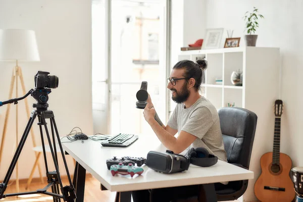 Hombre blogger tecnología celebración, apuntando a los auriculares durante la grabación de blog de vídeo o vlog sobre nuevos aparatos en el estudio en casa —  Fotos de Stock