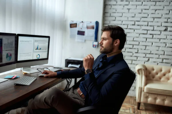 Vista lateral del joven empresario exitoso o gerente de ventas que analiza los datos financieros en la computadora, mirando las estadísticas en la pantalla de la PC mientras está sentado en su lugar de trabajo en la oficina moderna — Foto de Stock