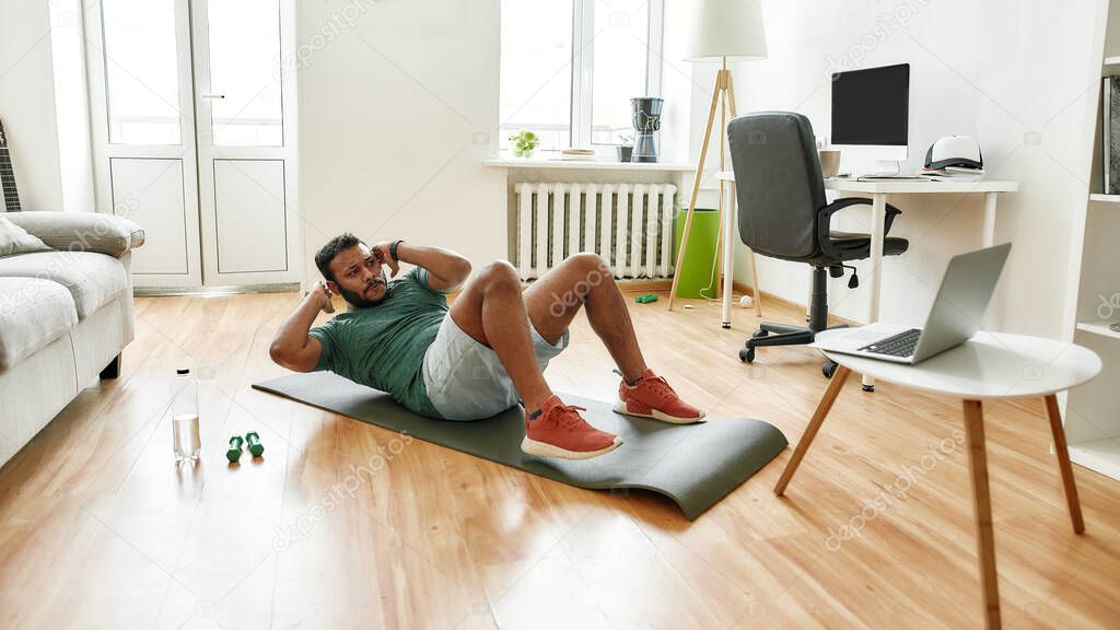 Your personal trainer. Male fitness instructor showing exercises while streaming, broadcasting video lesson on training at home using laptop. Sport, online gym concept