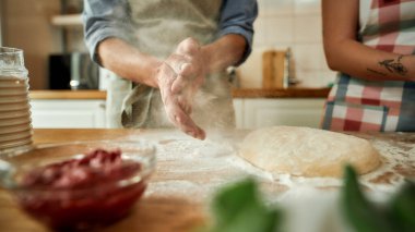 Birlikte pizza yapan bir çiftin görüntüsü. Önlüklü genç adam, kadın ona yardım ederken hamuru un kullanarak hazırlıyor. Hobi, yaşam tarzı