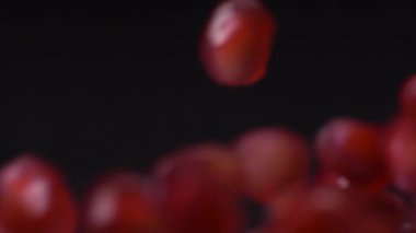Tohumları serbest bırakıyorum. Siyah arka planda düşen ve yuvarlanan nar tohumlarının süper yavaş çekimi. Nar tanecikleri 4K videosunu kapatır. Sağlıklı beslenme, meyve konsepti.