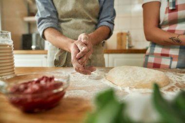 Birlikte pizza yapan bir çiftin görüntüsü. Önlüklü genç adam, kadın ona yardım ederken hamuru un kullanarak hazırlıyor. Hobi, yaşam tarzı