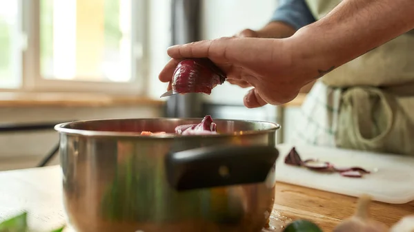 Närbild av händerna på människan, kock kock lägga lök till potten med hackade grönsaker samtidigt förbereda en måltid i köket — Stockfoto