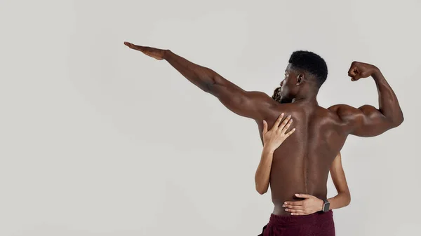 Deportiva mujer de raza mixta abrazando, tocando muscular afroamericano culturista espalda mientras posan juntos aislados sobre fondo gris. Deportes, entrenamiento, concepto de culturismo — Foto de Stock