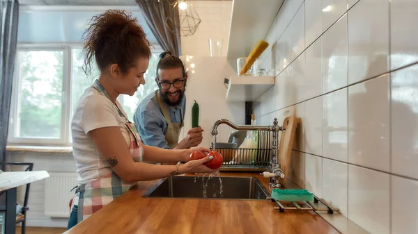 Feliz casal jovem lavar legumes na cozinha enquanto prepara os ingredientes para o jantar. Cozinhar em casa conceito — Fotografia de Stock