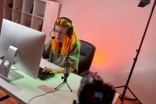 Podejmij wyzwanie. Kobiecy gracz sportowy, kobieta w słuchawkach wyglądająca na przestraszoną, grająca w gry wideo online na PC podczas nagrywania, filmująca vlog w domu — Zdjęcie stockowe