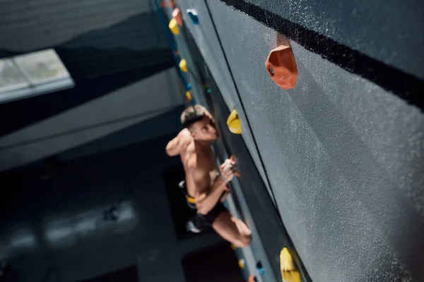 Muž v bezpečnostním vybavení a trénink postroje na umělé lezecké stěně uvnitř, zaměření na balvan — Stock fotografie
