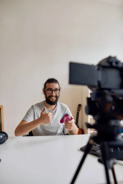 Blogger de tecnologia masculina em óculos mostrando polegares para cima, segurando joystick controlador de jogo durante a gravação de vídeo blog ou vlog sobre novos gadgets em casa — Fotografia de Stock