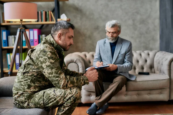 Healing. Thoughtful middle aged military man looking away during therapy session with psychologist. Soldier suffering from depression, psychological trauma. PTSD concept