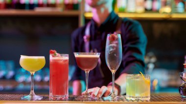 Keyfiniz için. Klasik kokteyller, bar tezgahında alkollü içecekler ve arka planda profesyonel bir barmen duruyor.